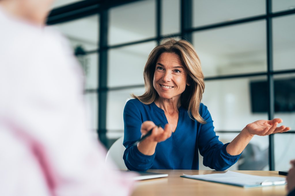An executive in a blue blouse making a point across a meeting table