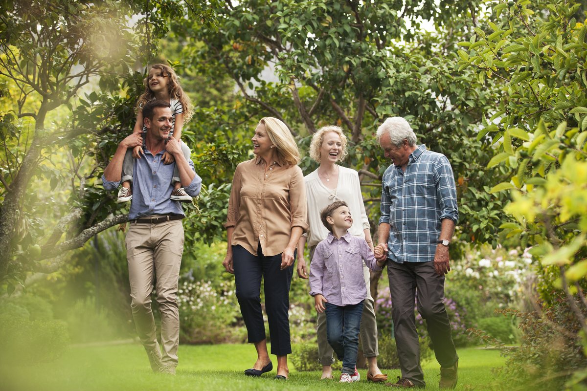 Three generations walking together through a garden, a child riding on her father's shoulders