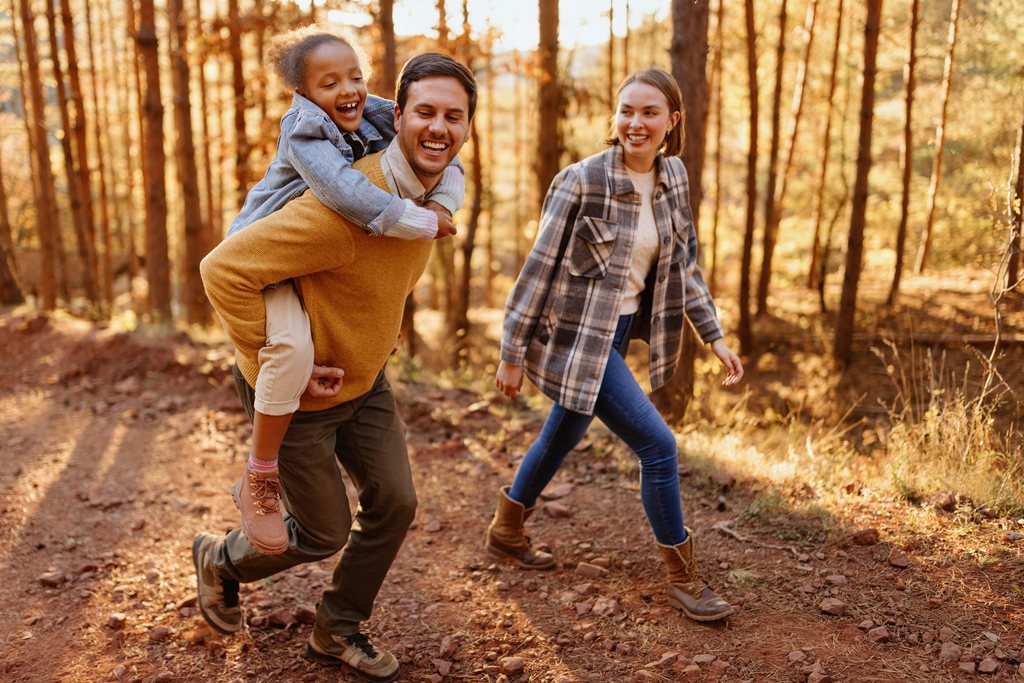 A young family walking a forest trail in autumn, a child riding on her father's back